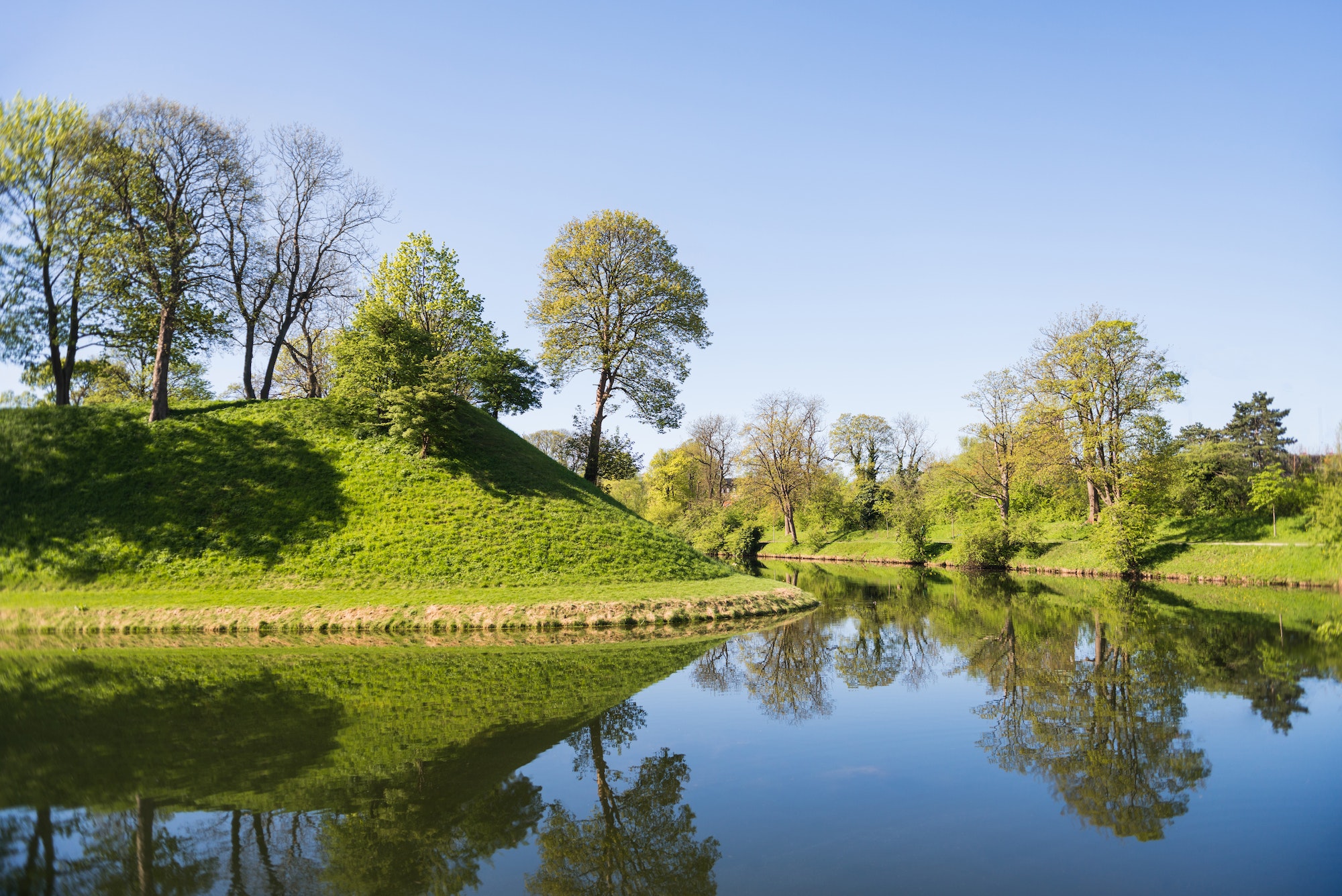 beautiful green hills, trees and bushes reflected in water, copenhagen, denmark