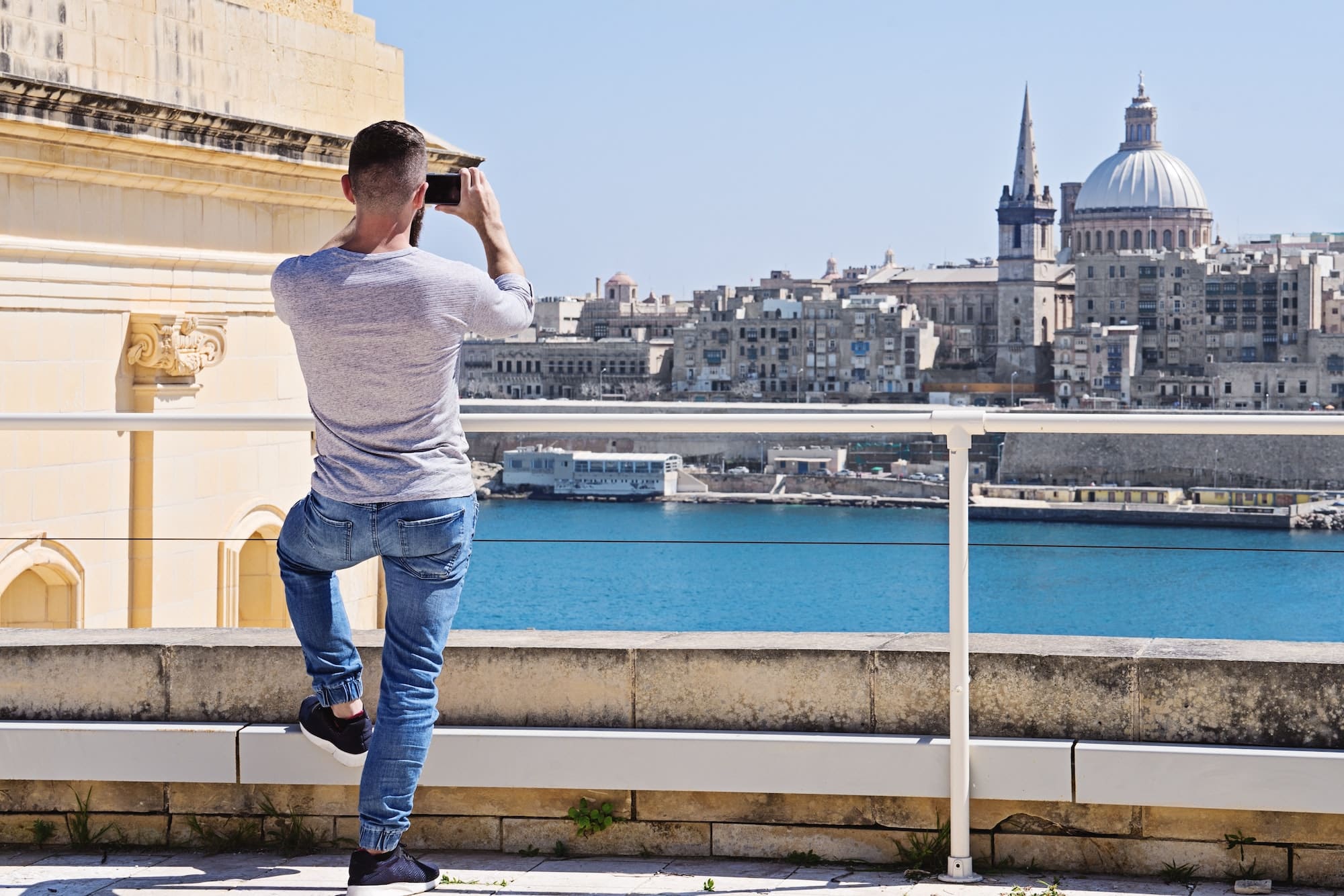 Caucasian student man behind with smartphone take photo of Valletta skyline cityscape