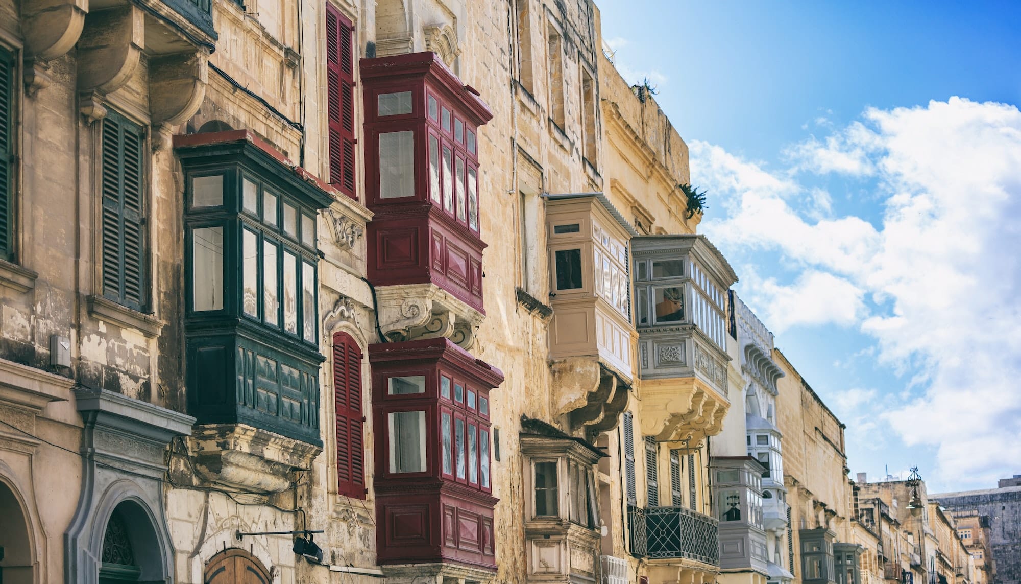 Malta, Valletta, building facade with covered balconies, with blue sky background, perspective view