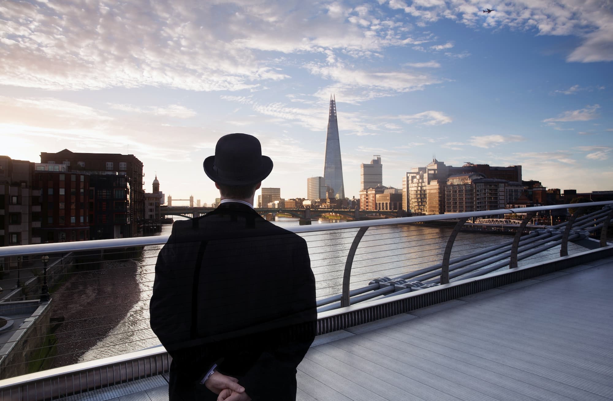 Man in bowler hat standing on Millennium Bridge over the River Thames in London