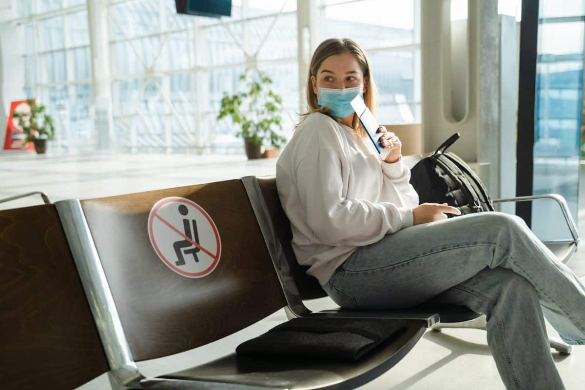 Woman tourist with mask with flight tickets and sitting in a socially distanced chair
