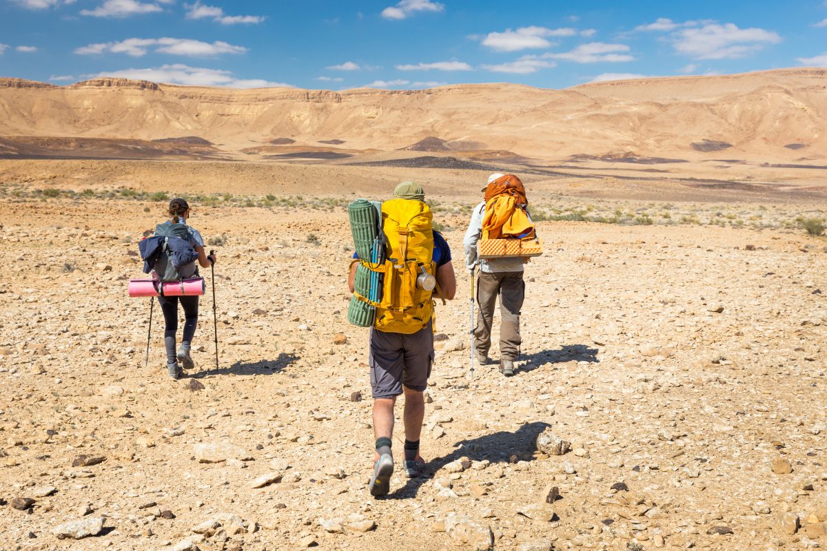 Three backpackers walking stone desert trail.